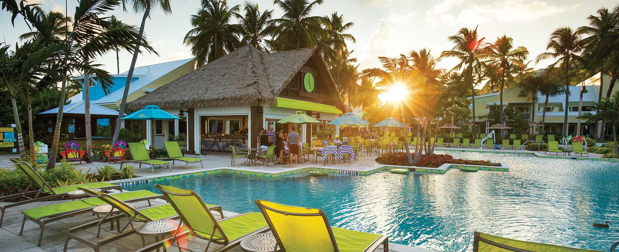 The sun sets on the pool, tiki bar, and bright green pool chairs at Margaritaville Vacation Club by Wyndham - St. Thomas.