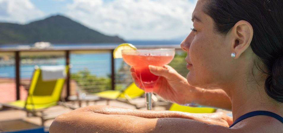 Dark-haired woman looks out over the ocean with a pink margarita in hand, relaxing at a Margaritaville Vacation Club resort.